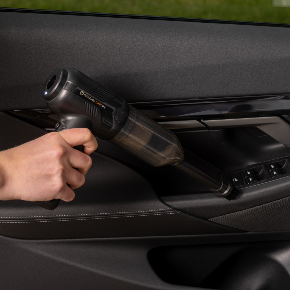 Eine Hand reinigt die schwarze Autotür mit einem kleinen Handstaubsauger.