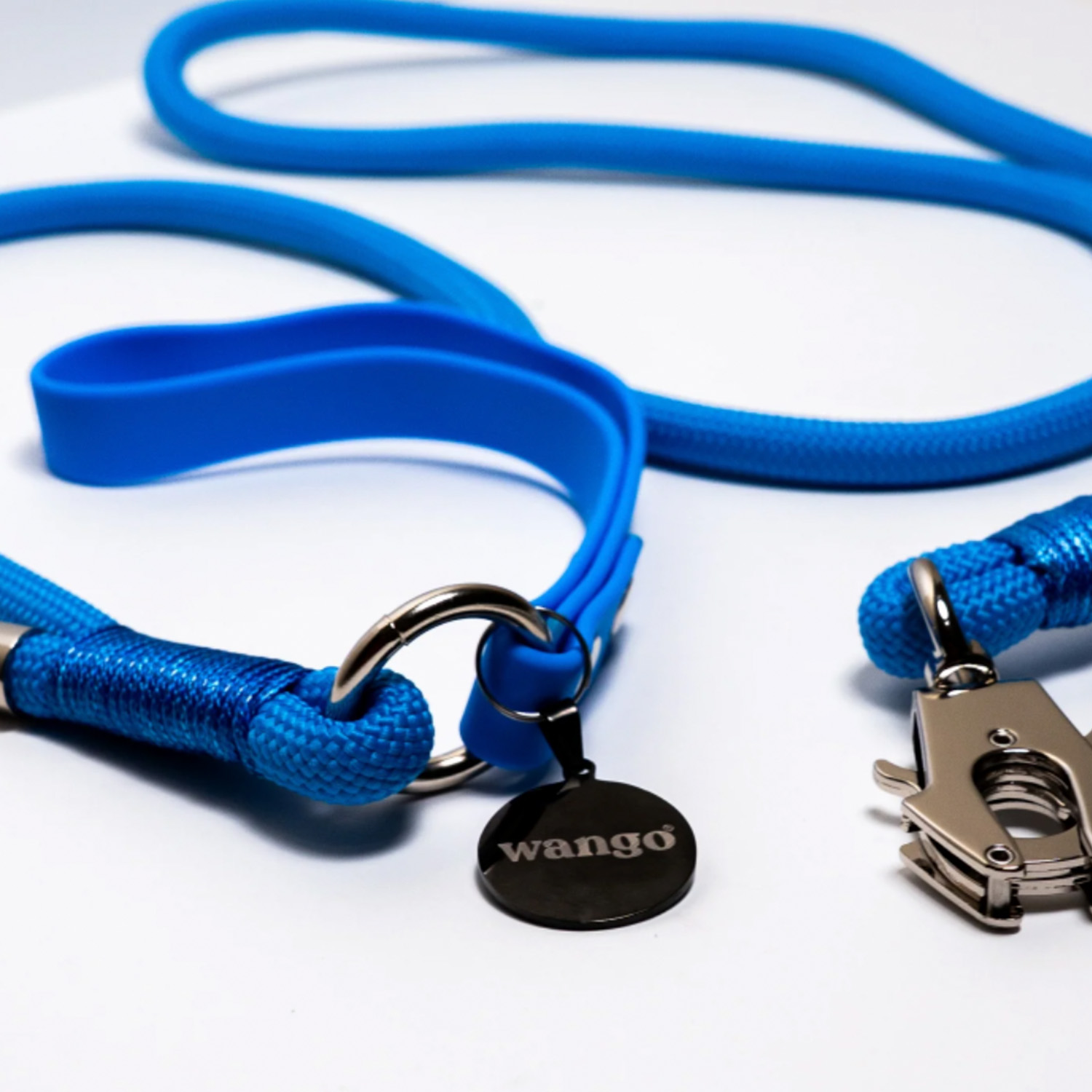 Un collar y correa de perro azul con un anillo plateado y una etiqueta negra redonda wango sobre fondo blanco.