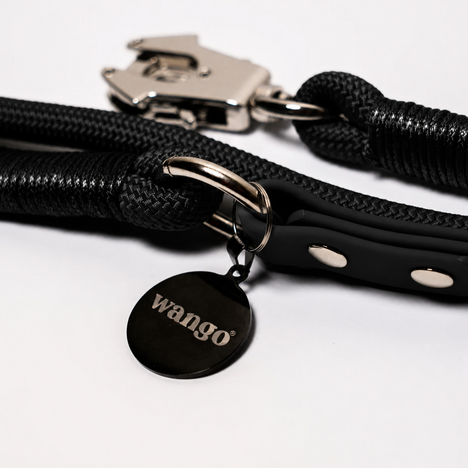 Una correa de perro negra trenzada con herrajes de metal plateado y una placa redonda con "wango".