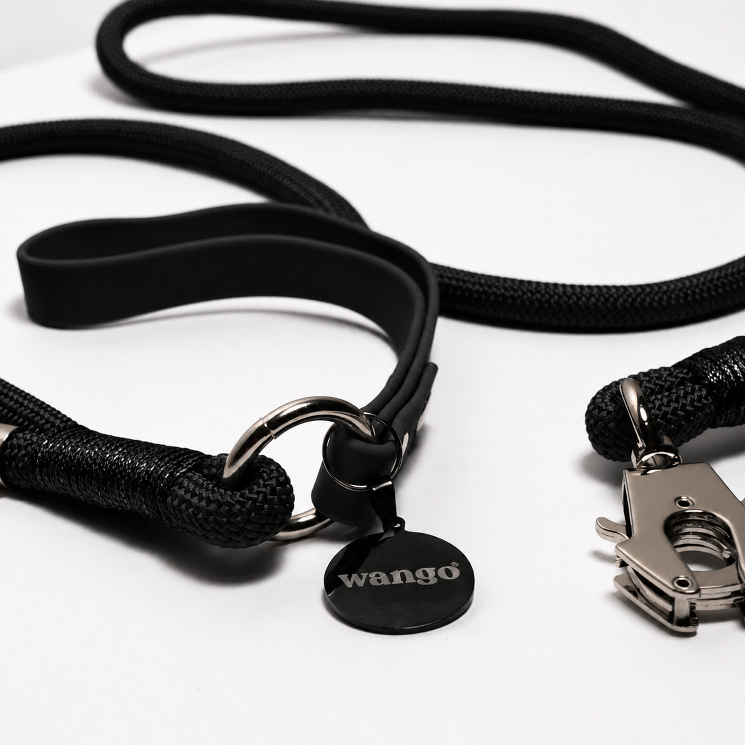 Una correa de perro negra con cierre de metal y placa redonda con "wango" sobre fondo blanco.