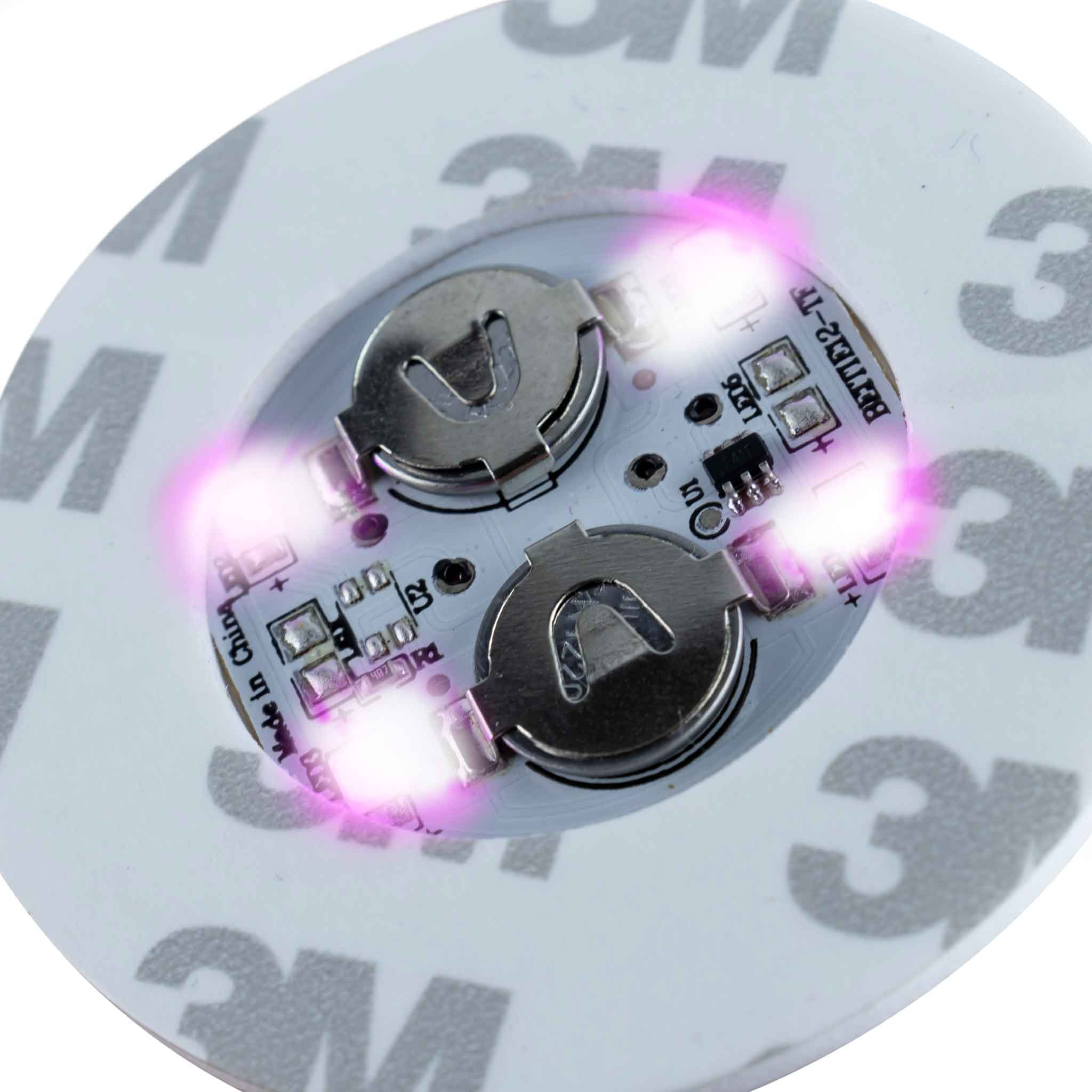 Runde elektronische Platine mit zwei Silberknopfbatterien und vier leuchtenden Pink-LEDs auf Klebeband.