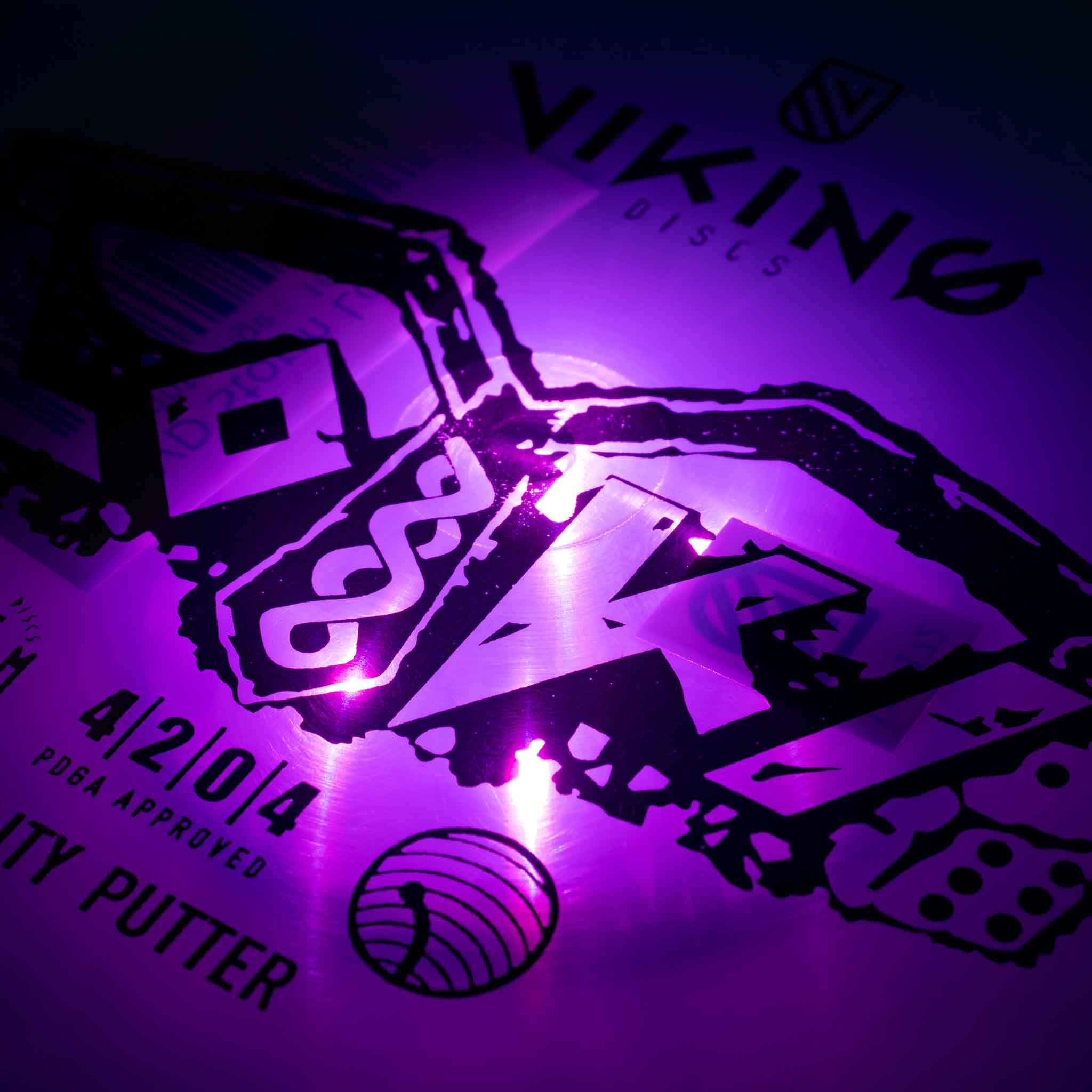 Eine lila Disc-Golf-Scheibe zeigt das Viking-Discs-Logo und Flugzahlen bei hellem lila Licht.