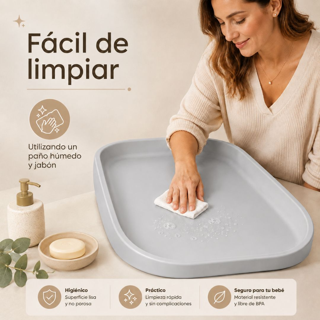 Una mujer limpia un cambiador gris claro con un paño húmedo junto a un dispensador de jabón y pastilla.