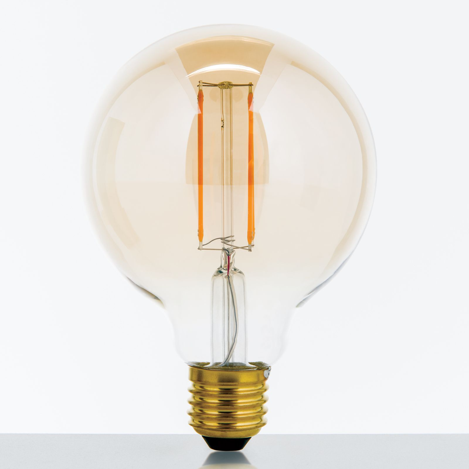 Große, runde LED-Glühbirne mit sichtbaren orangefarbenen Filamenten und goldenem Schraubsockel auf hellem Grund.