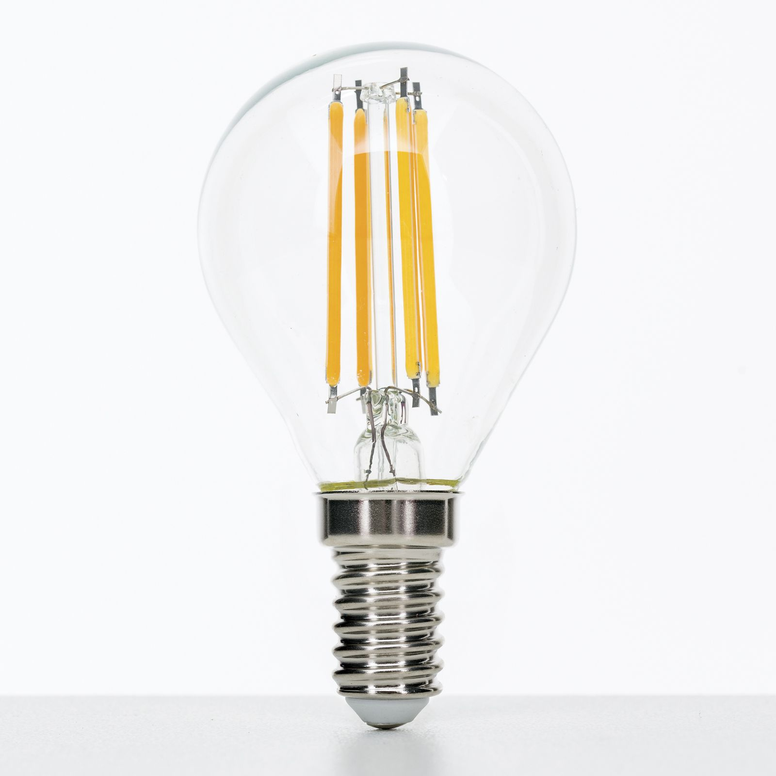 Eine transparente LED-Glühlampe mit sichtbaren gelben Fäden auf weißem Hintergrund.