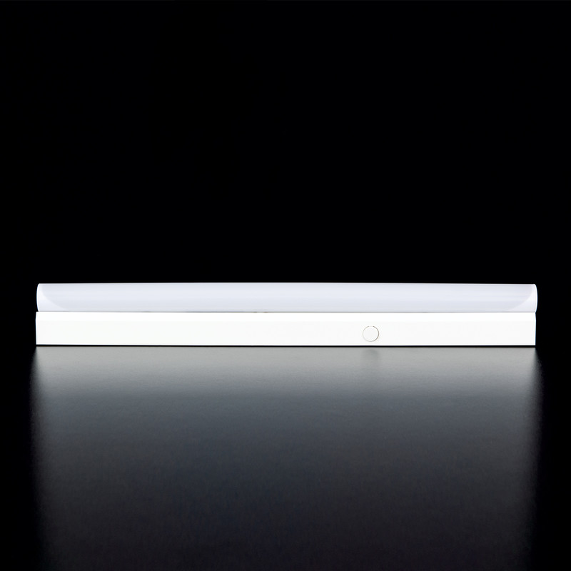 Eine schmale weiße LED-Unterleuchtlampe mit einem runden Schalter auf einer dunklen Oberfläche.