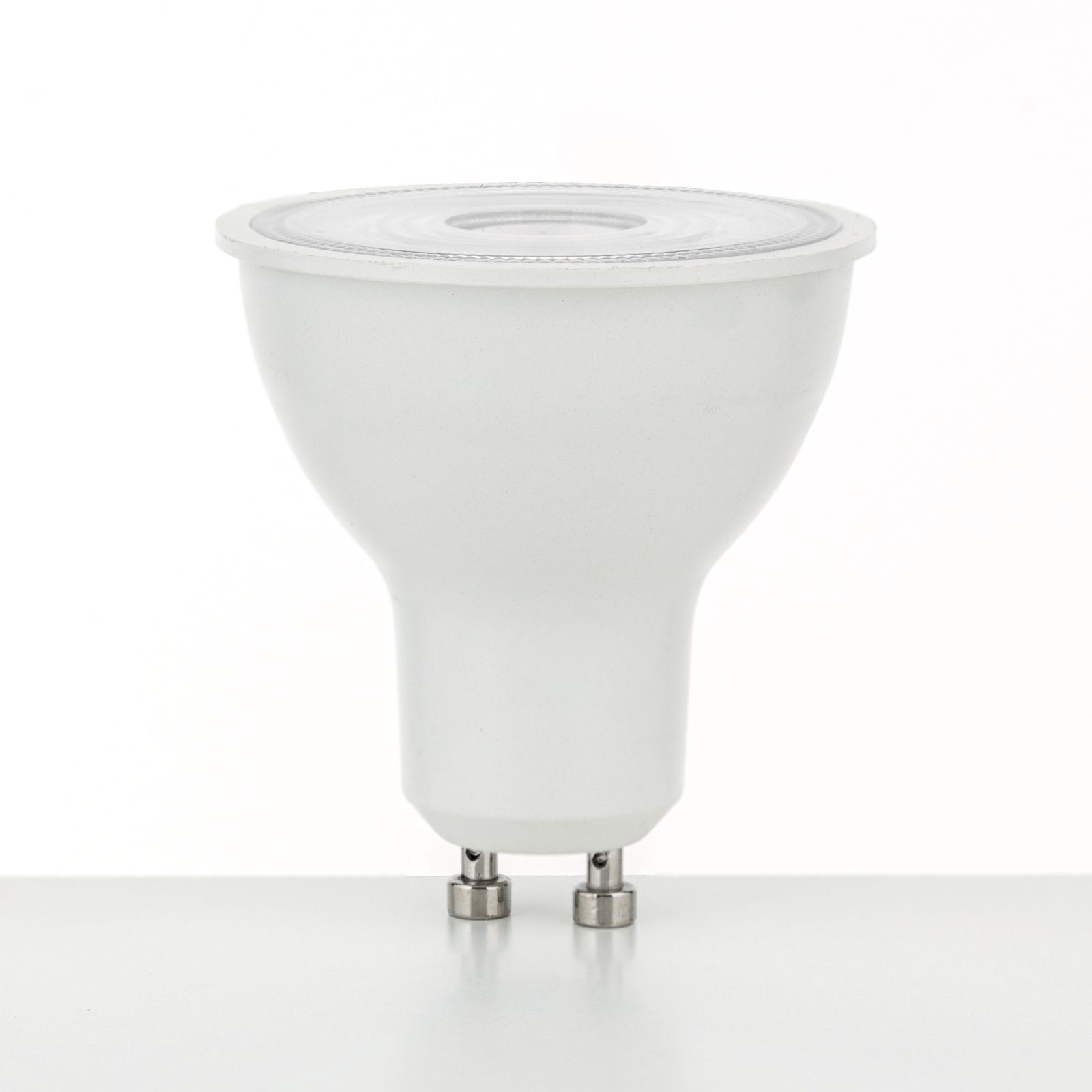 Eine weiße LED-Reflektorlampe mit zwei Pins steht auf einer weißen Oberfläche vor hellem Hintergrund.