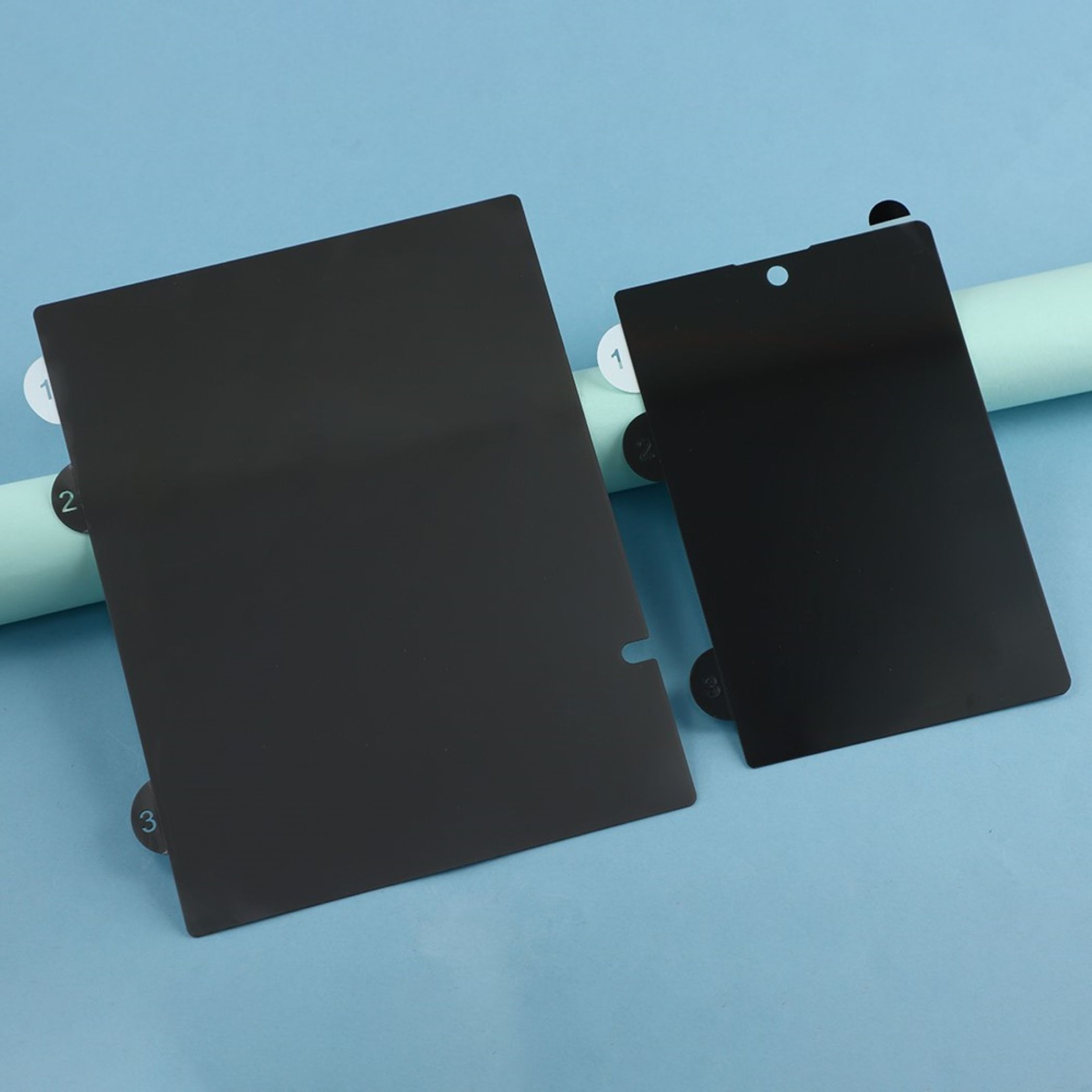 Zwei schwarze Schutzfolien liegen auf einer hellblauen Unterlage.