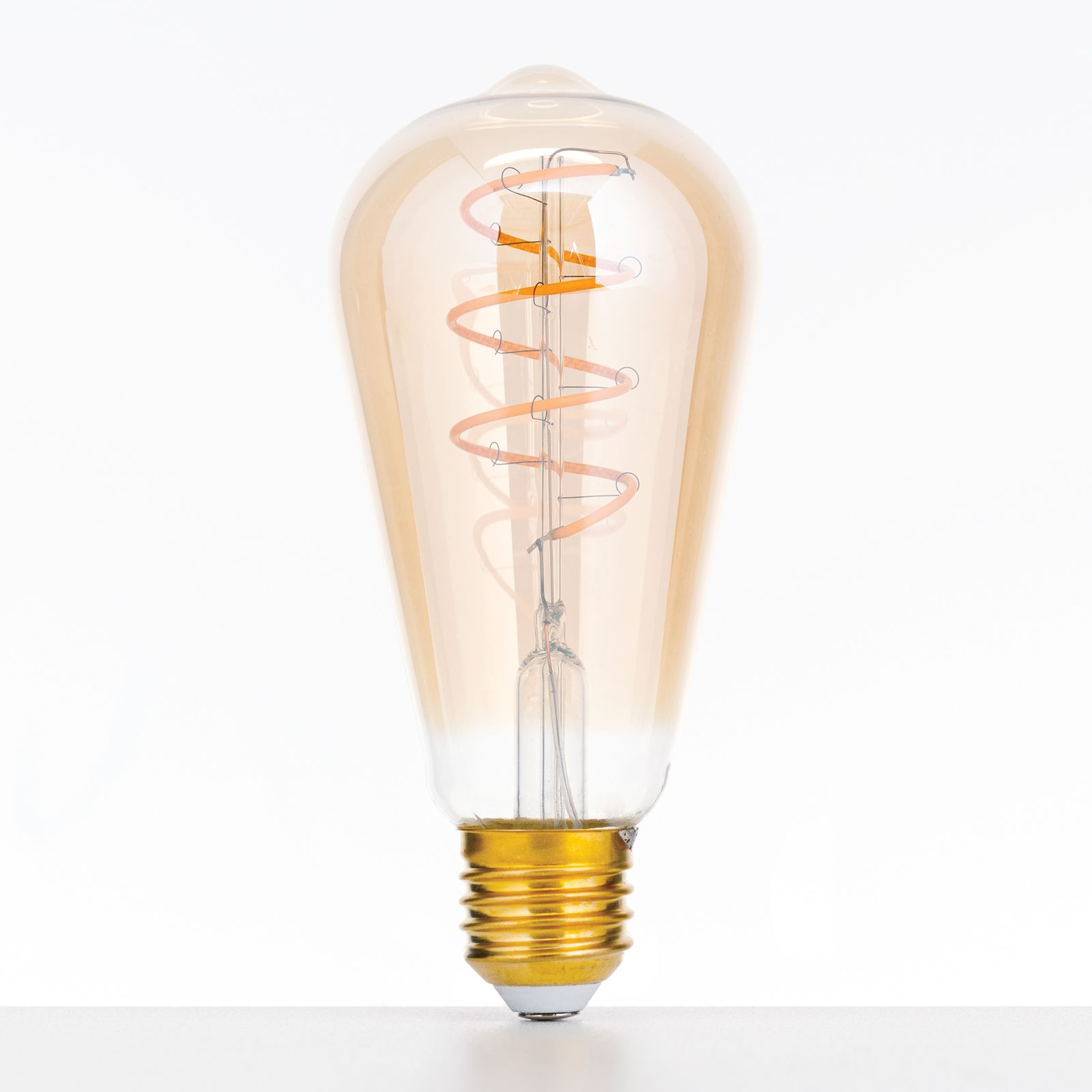 Eine bernsteinfarbene Vintage-LED-Glühbirne mit spiralförmigem Leuchtdraht auf weißem Hintergrund.