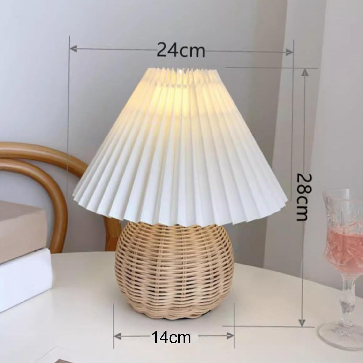 Eine Rattantischlampe mit weißem Plissérschirm auf weißem Tisch mit Maßangaben: 24cm Breite, 14cm Basis, 28cm Höhe.