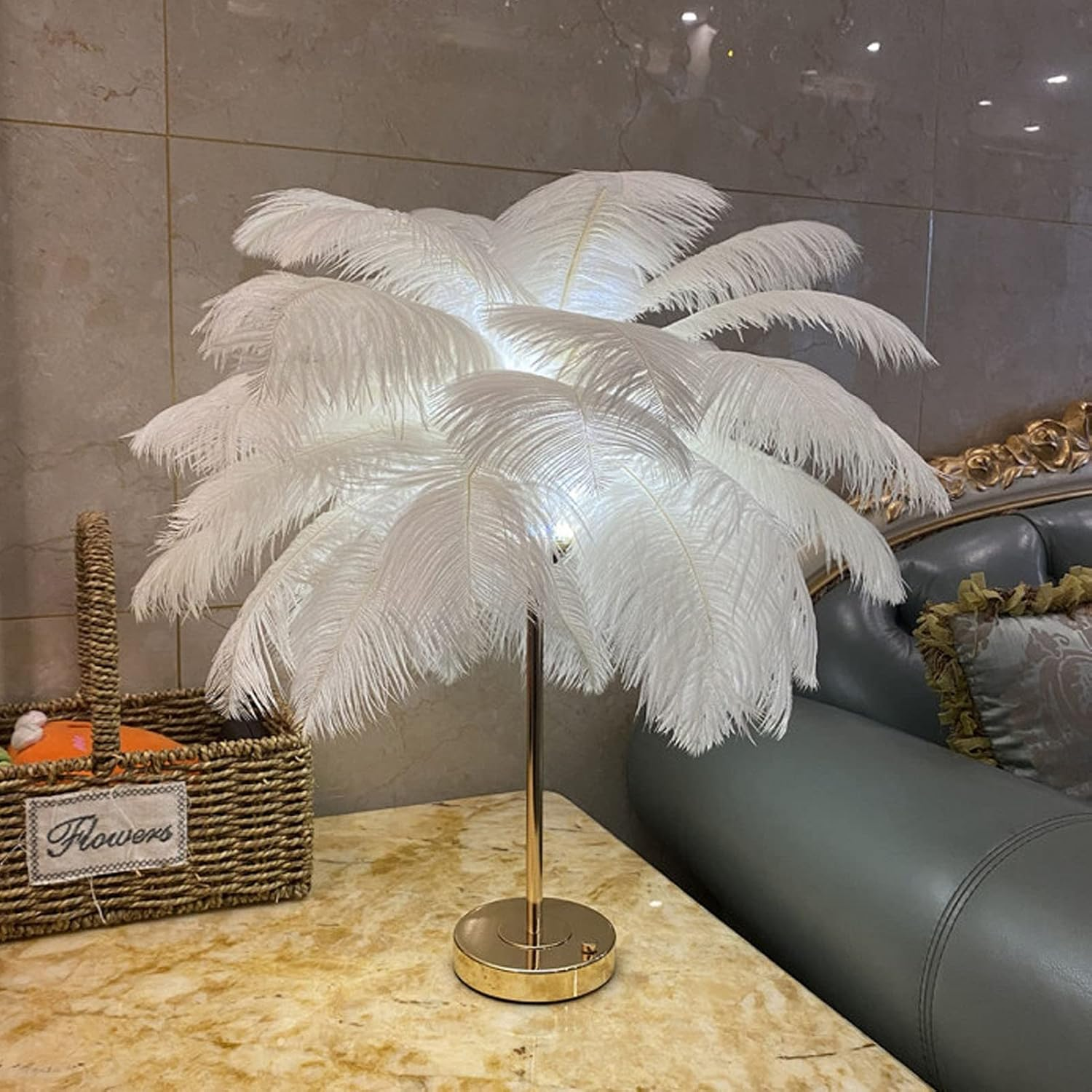 Dekorative Tischlampe mit weißen Straußenfedern auf Marmortisch, mit Korb und grauem Sofa im Hintergrund.