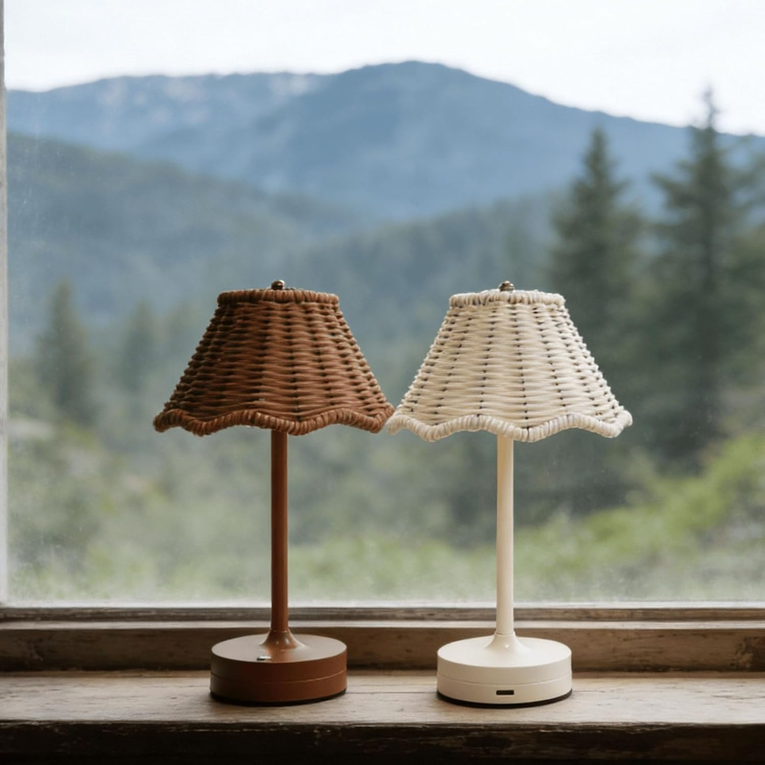 Zwei kleine Lampen mit gewebten Schirmen stehen auf einer Fensterbank vor einer Bergkulisse.