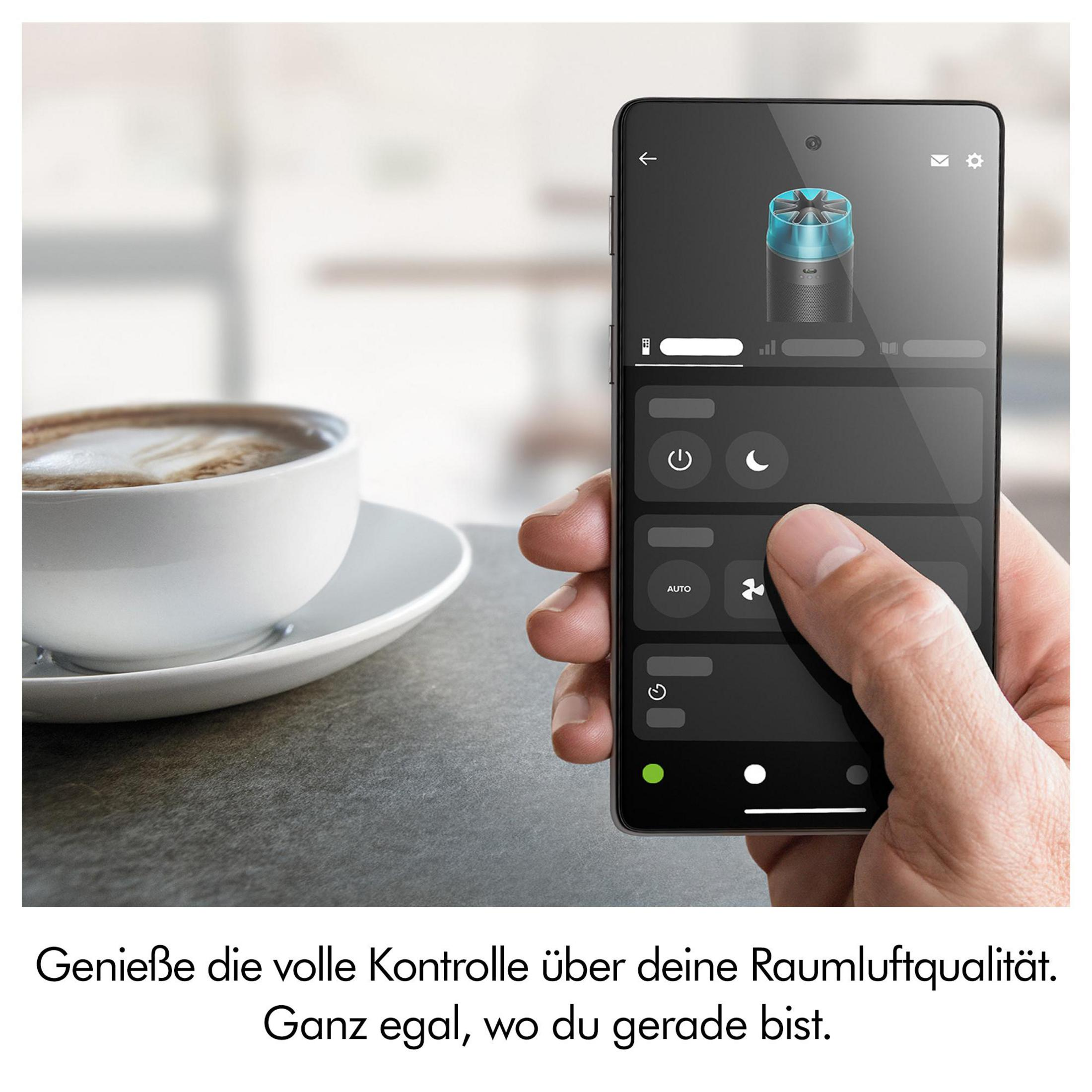 Mano che tiene uno smartphone con app di controllo aria vicino a una tazza di caffè.