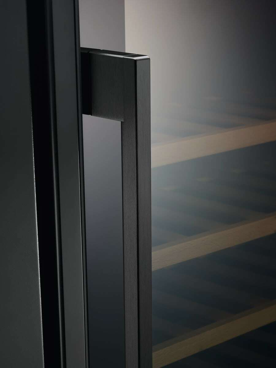 Primer plano de una manija de puerta negra en una vinoteca con estantes de madera al fondo.