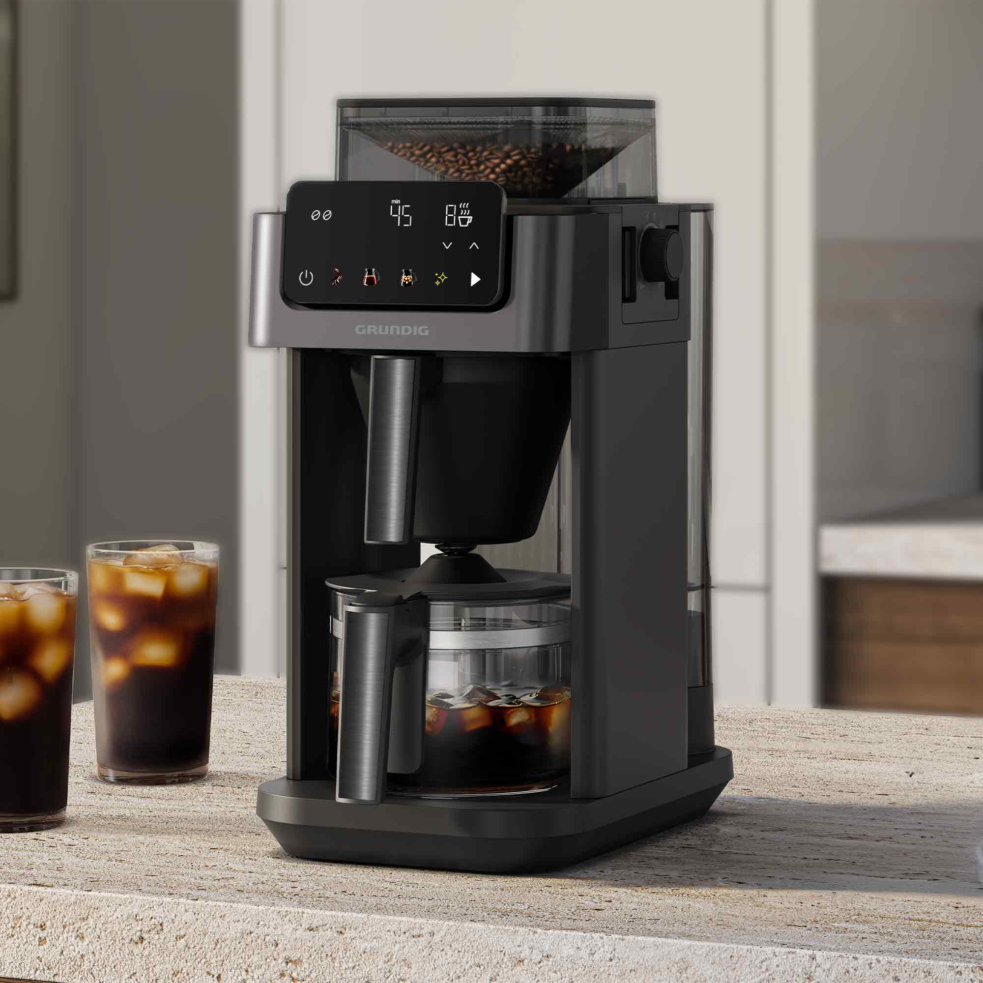 Moderne graue Kaffeemaschine auf einer Küchentheke mit zwei Gläsern Eiskaffee links.
