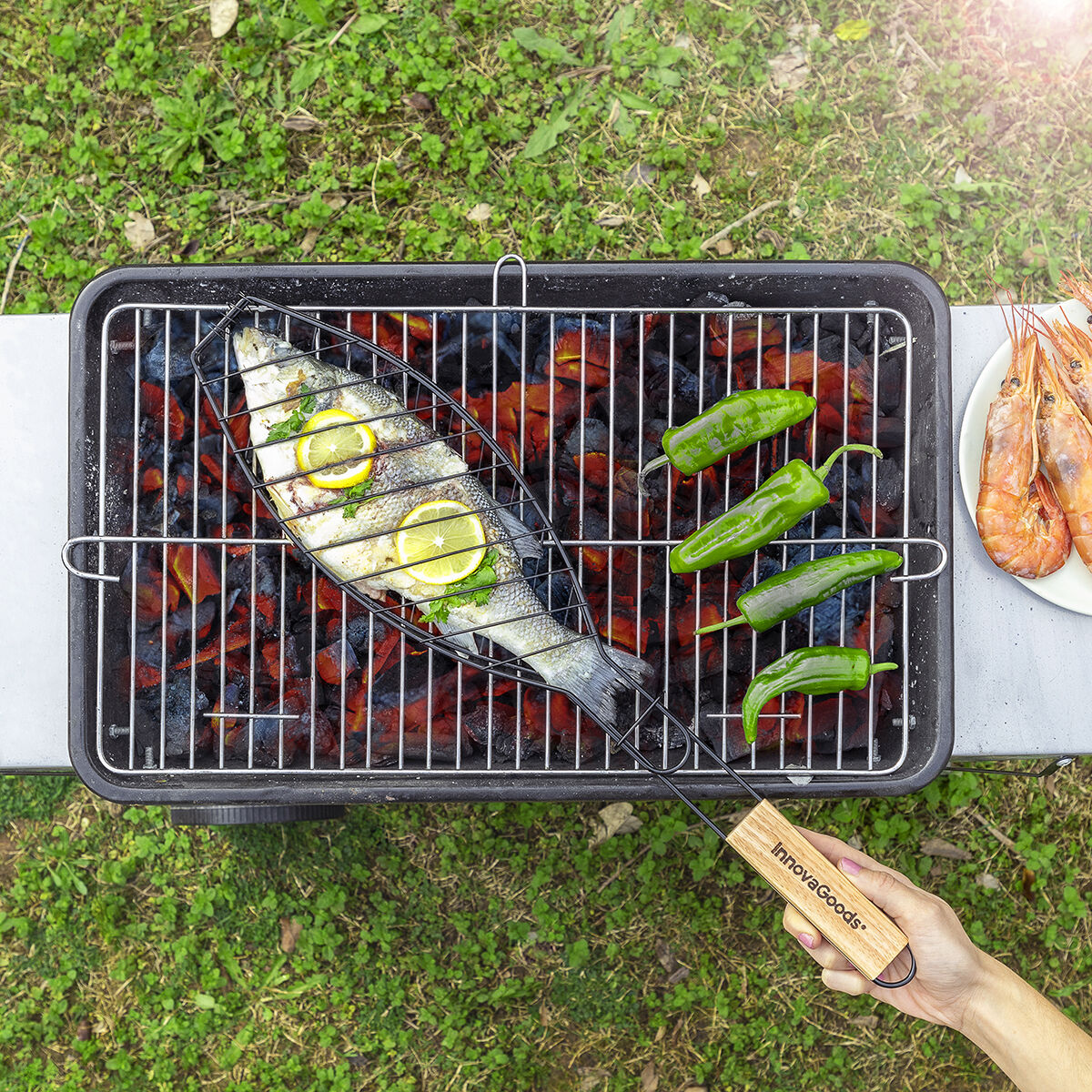 Ein ganzer Fisch mit Zitronenscheiben und vier grüne Paprika grillen auf Kohlen.