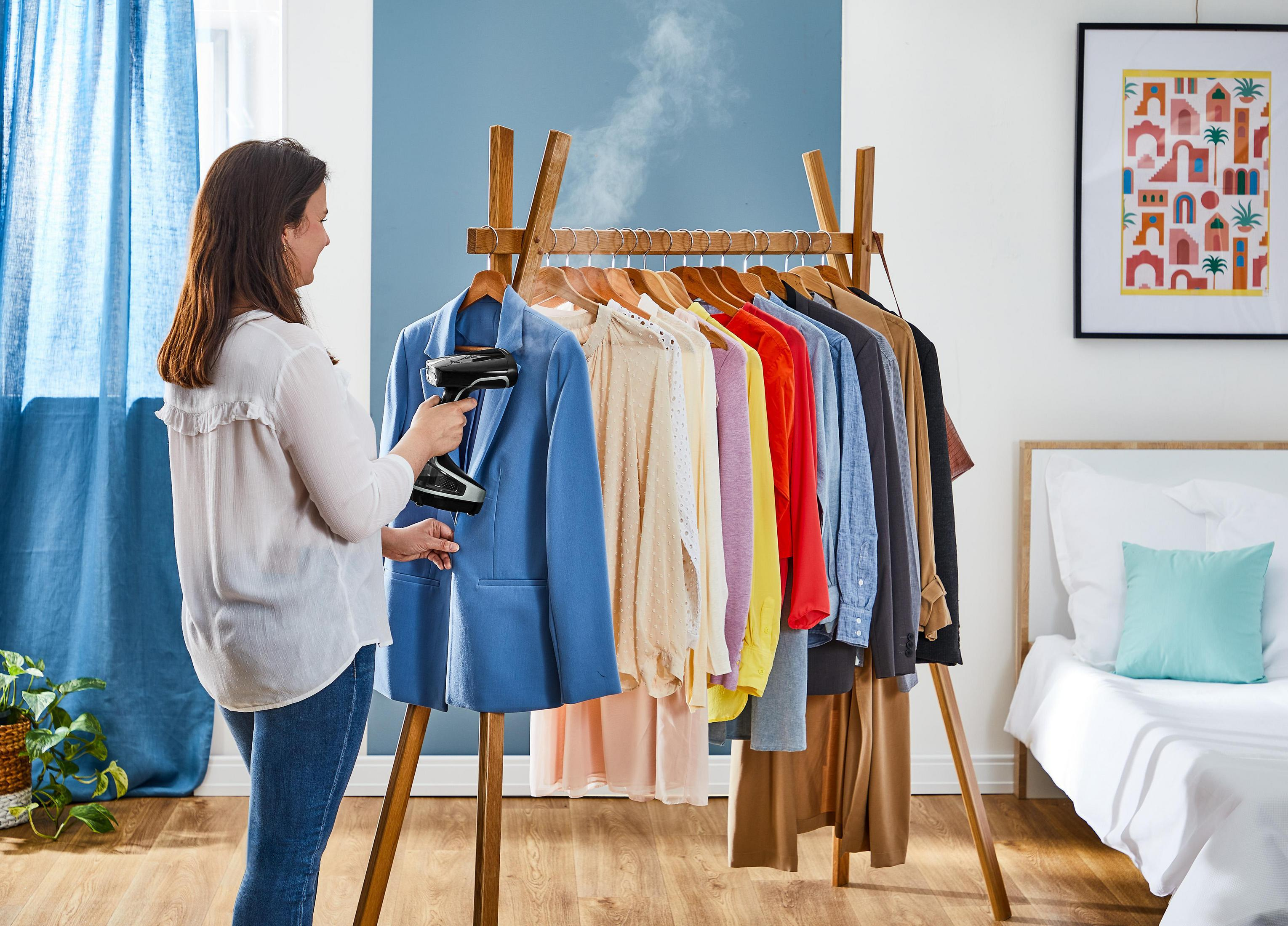 Eine Frau in weißer Bluse bedient einen Handdampfgarer an einer blauen Jacke auf einem Holzständer.