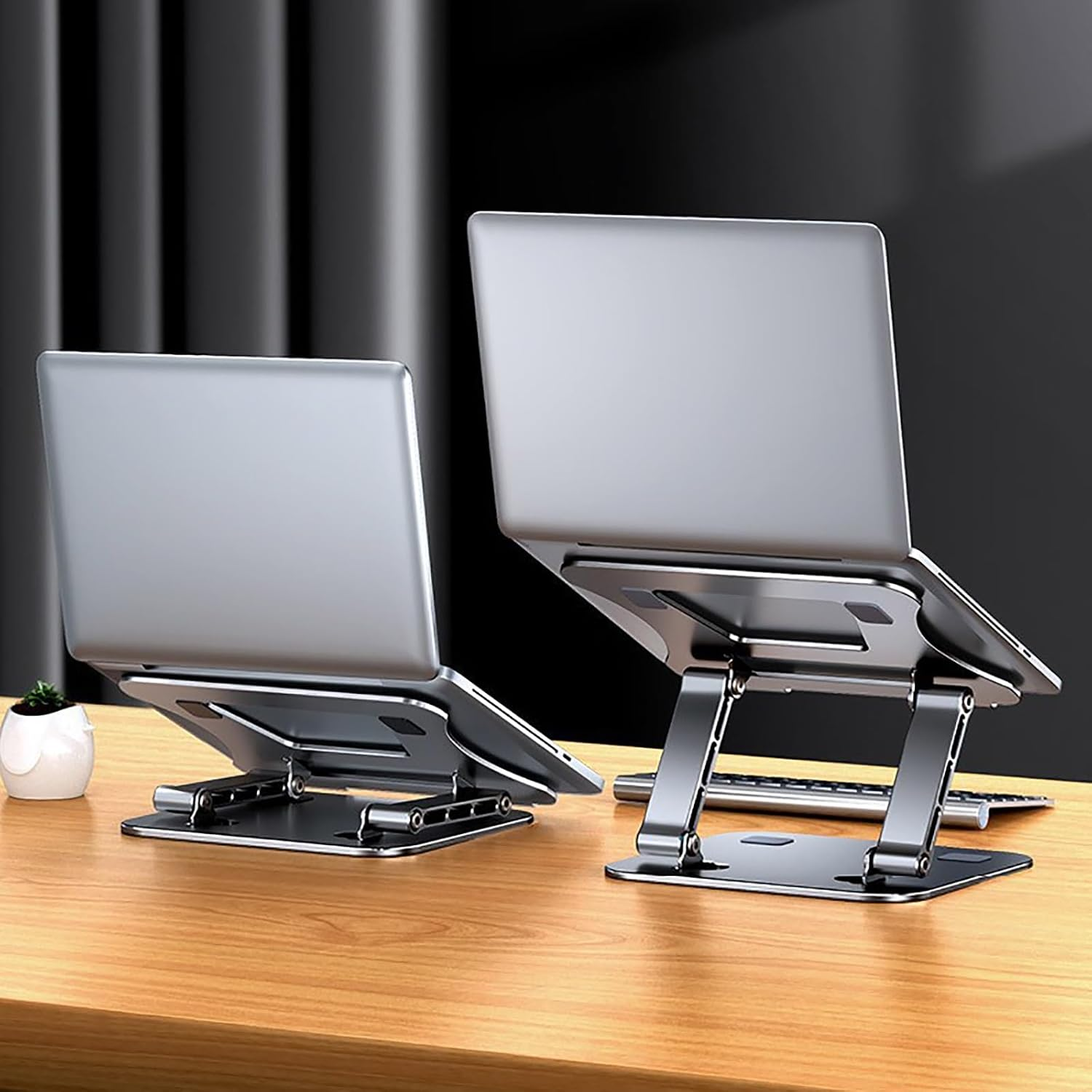 Zwei silberne Laptops auf verstellbaren Metallständern auf einem Holztisch, im Hintergrund dunkle Vorhänge.