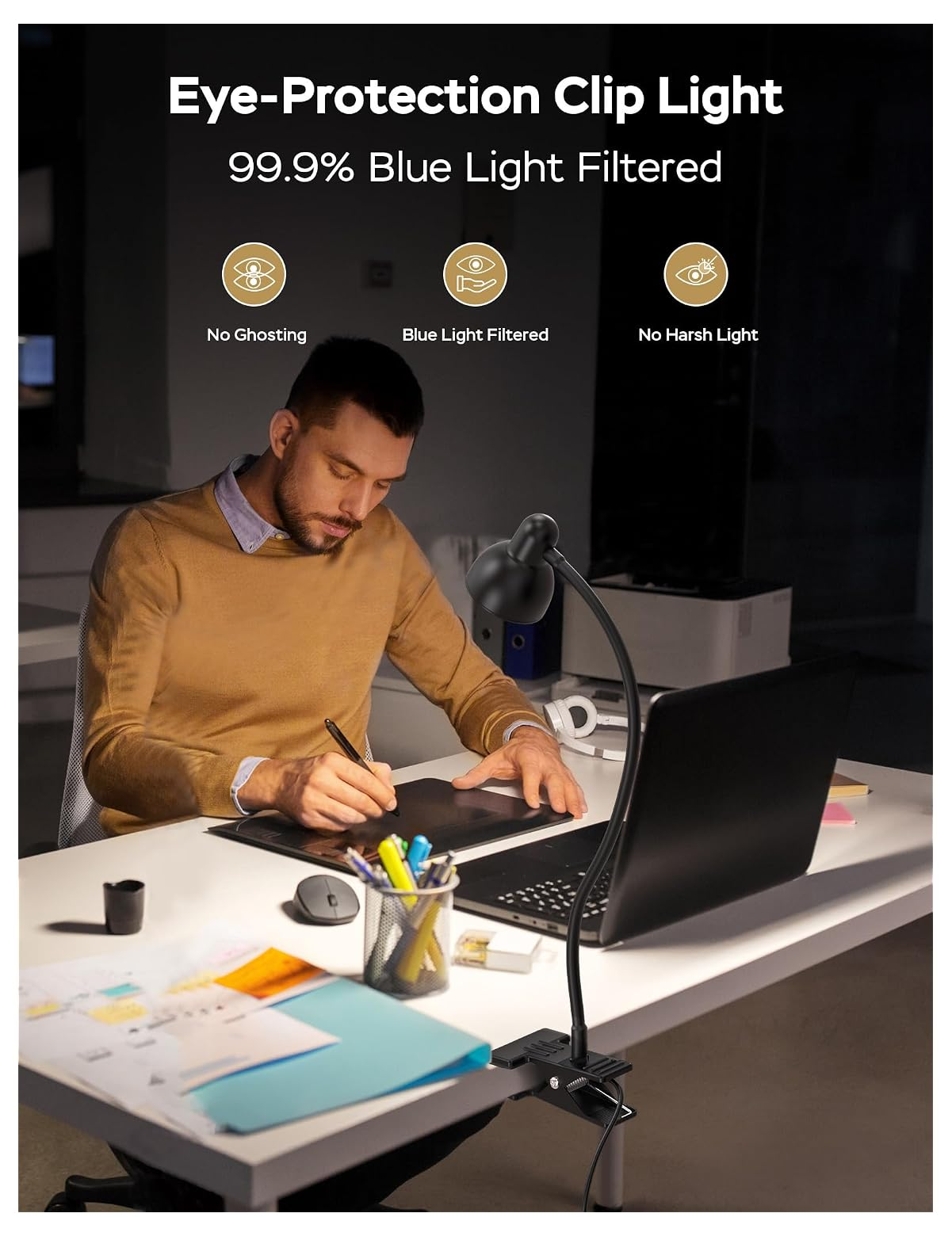 Ein Mann zeichnet an einem Schreibtisch mit Laptop, beleuchtet von einer schwarzen Klemmleuchte.