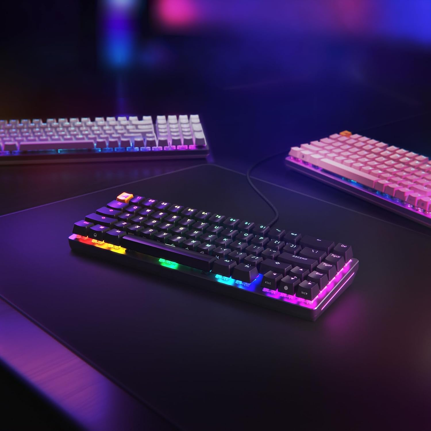 Renkli RGB arka aydınlatmalı üç mekanik klavye bir masada düzenlenmiştir.