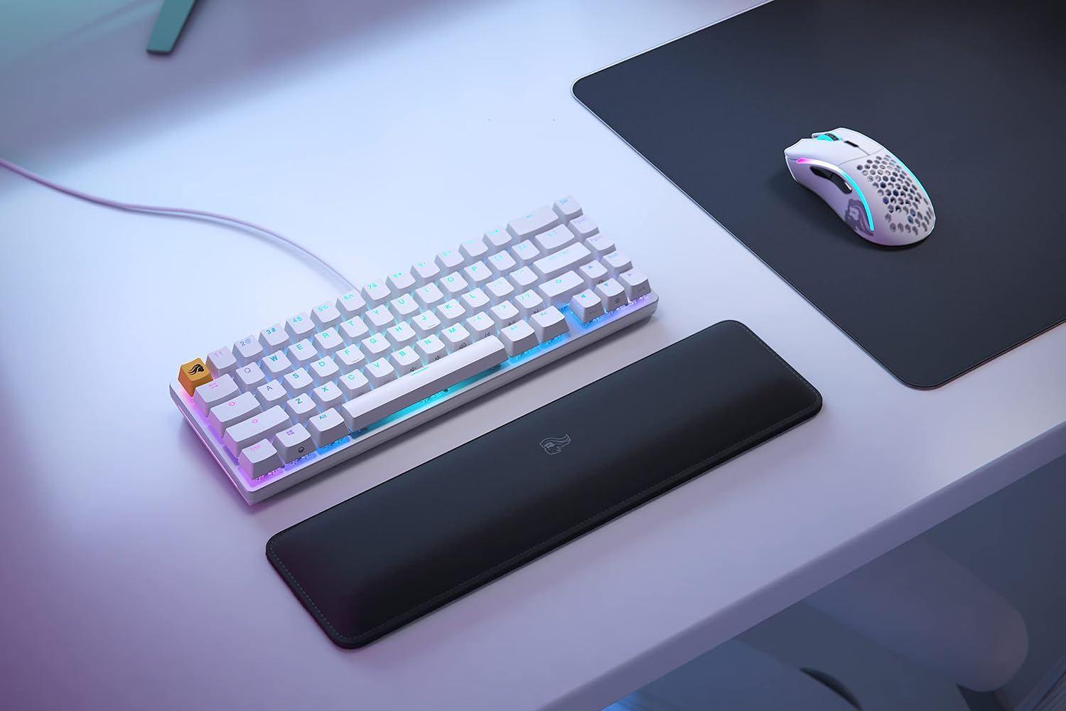 RGB aydınlatmalı beyaz bir klavye, bilek desteği ve siyah mouse pad üzerinde beyaz bir fare.