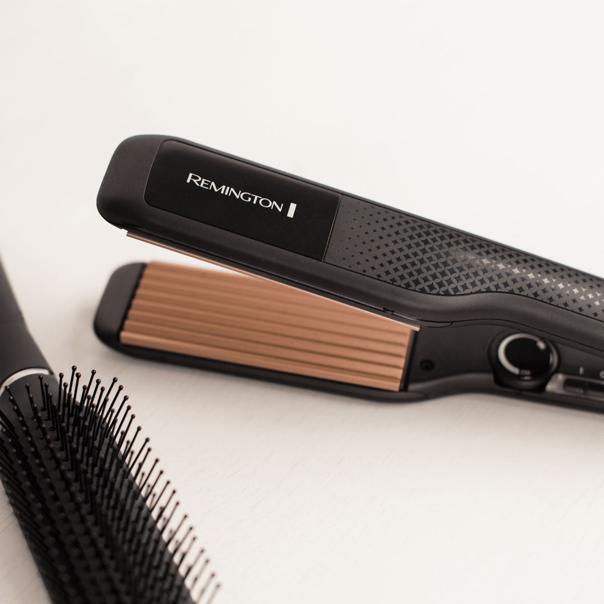 Una piastra per capelli Remington nera e una spazzola su una superficie chiara.