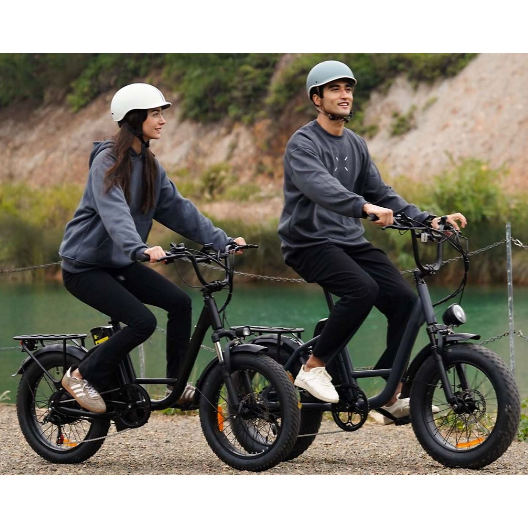 Due persone con caschi e vestiti scuri guidano e-bike nere lungo la riva di un fiume.