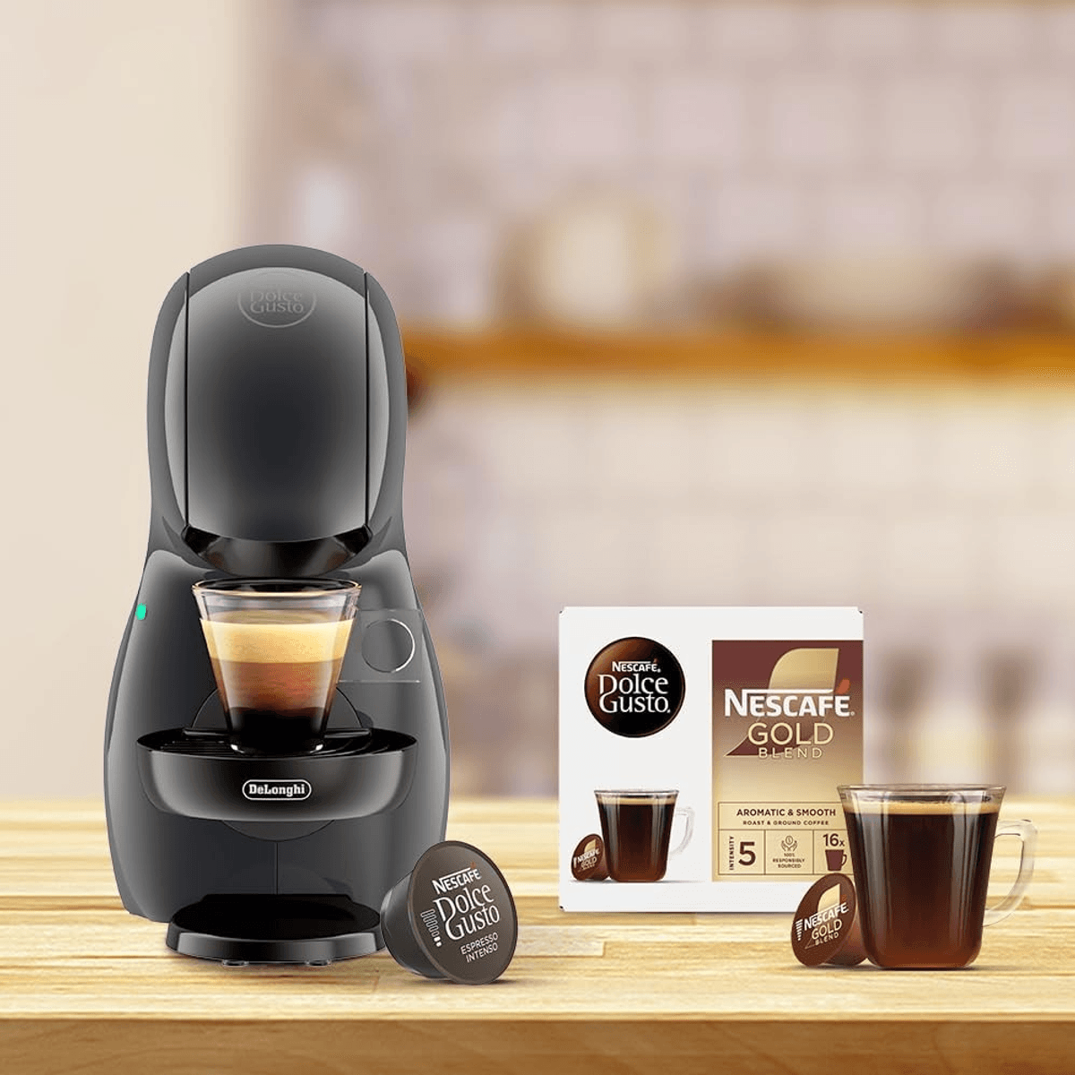 Una macchina da caffè nera Dolce Gusto, capsule, una scatola Nescafé Gold Blend e tazze.