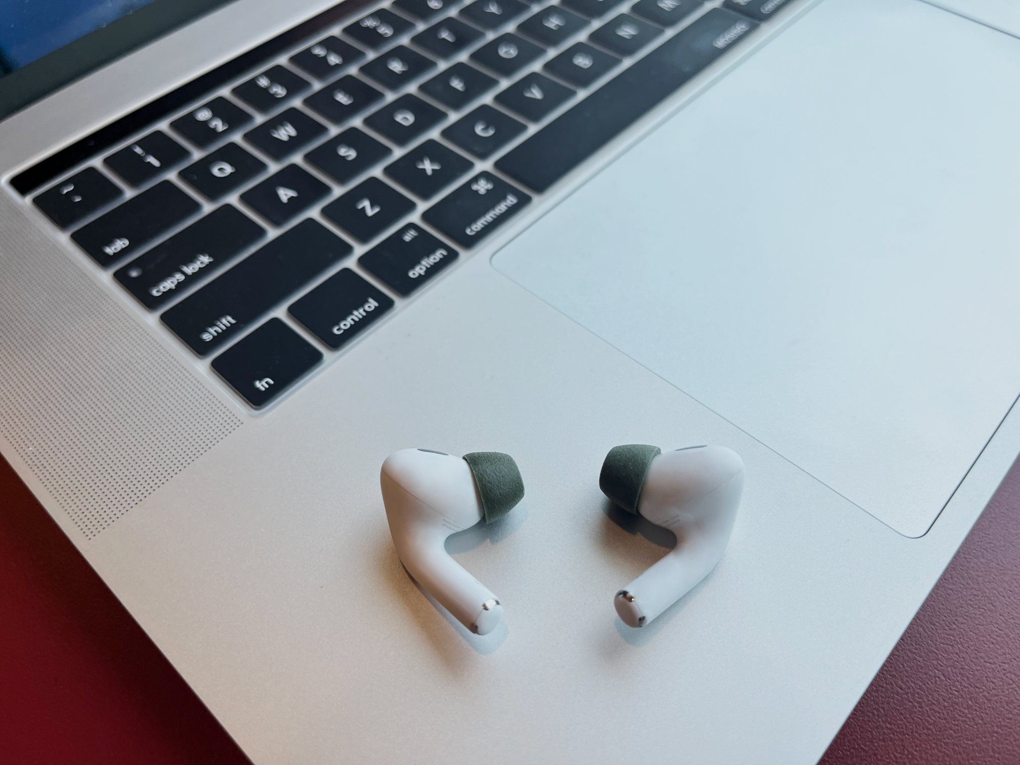 Weiße In-Ear-Kopfhörer mit grauen Silikonaufsätzen liegen auf der Handballenauflage eines silbernen Laptops.