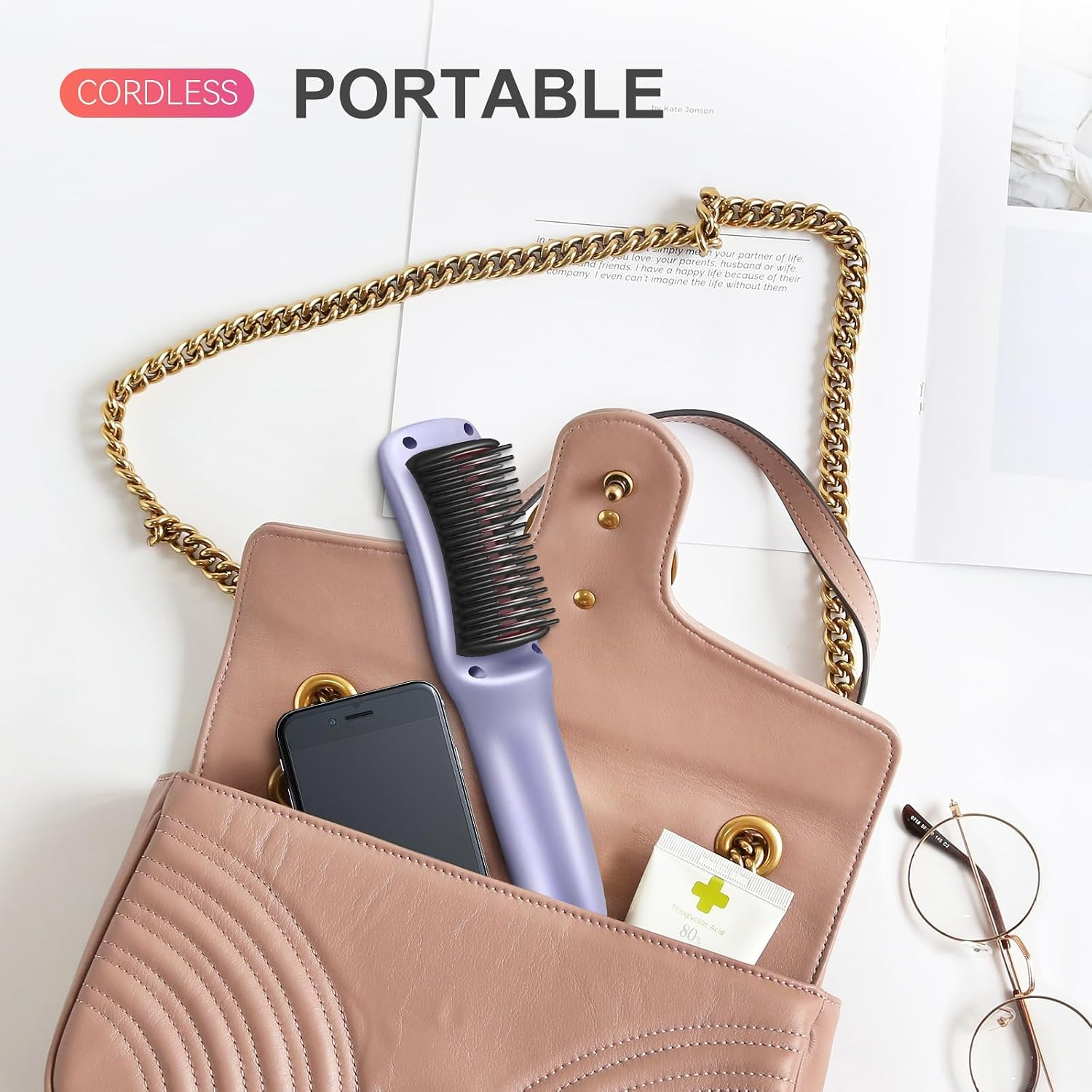 Eine lila tragbare Haarglätterbürste, ein Handy und eine Cremetube in einer rosa Handtasche mit Goldkette.