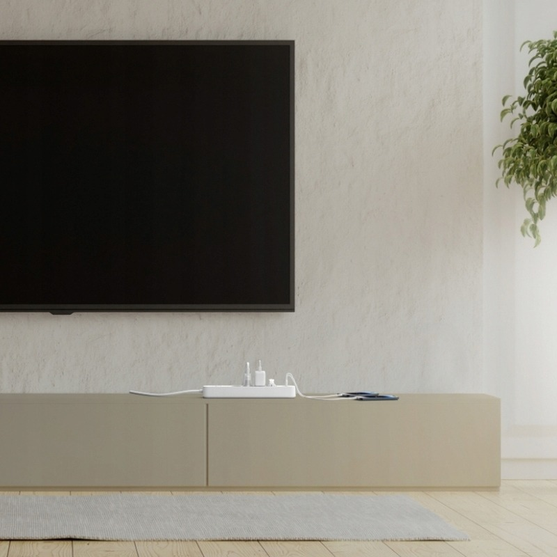 Una TV bianca è appesa a una parete beige sopra un mobile basso. Una ciabatta elettrica si trova sul mobile.