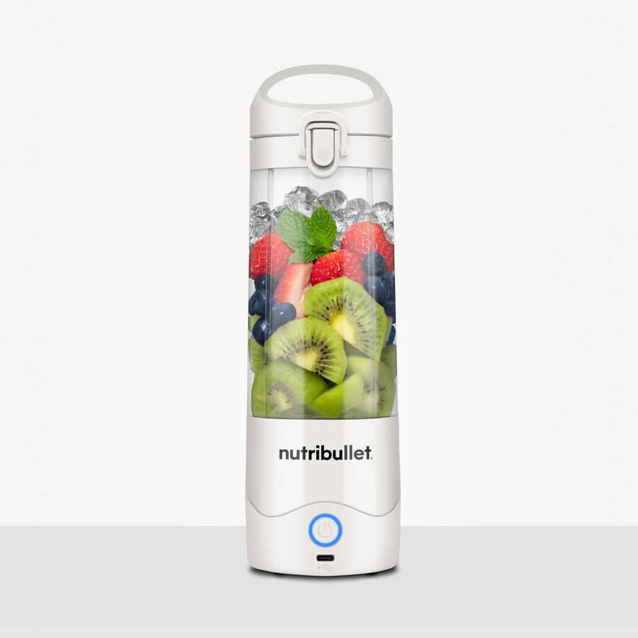 A white Nutribullet portable blender filled with ice, kiwi, strawberries, blueberries, and mint leaves.