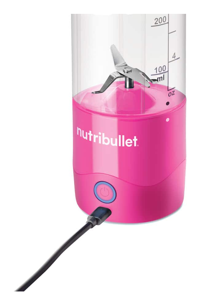 A pink Nutribullet blender with stainless steel blades and a connected charging cable against a white background.
