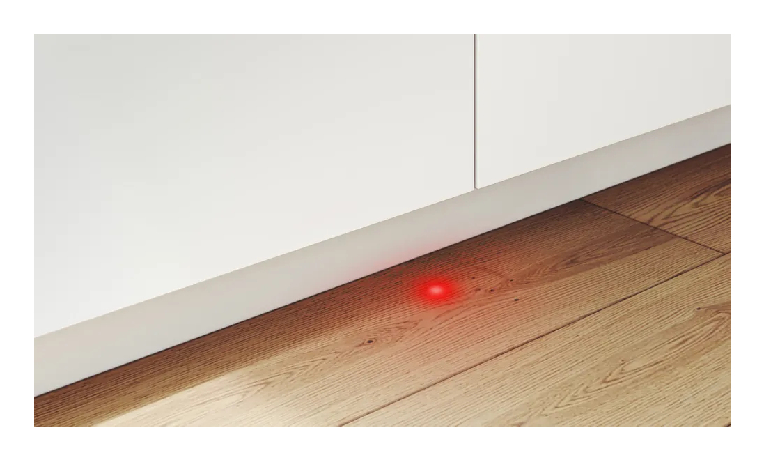 Un punto di luce rossa brilla sul pavimento in legno sotto i mobili bianchi.