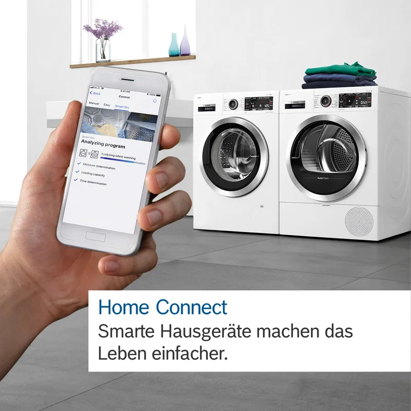 Hand hält Smartphone mit Waschmaschinen-App vor zwei weißen Bosch-Waschgeräten.