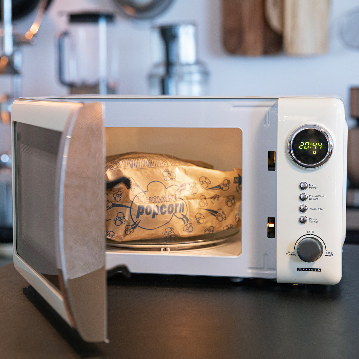 Un micro-ondes blanc avec la porte ouverte contient un sachet de pop-corn pour micro-ondes dans une cuisine.