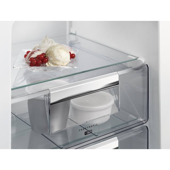 Gelato con bacche rosse su un piatto nel ripiano superiore di un frigorifero bianco e contenitori bianchi nel cassetto.