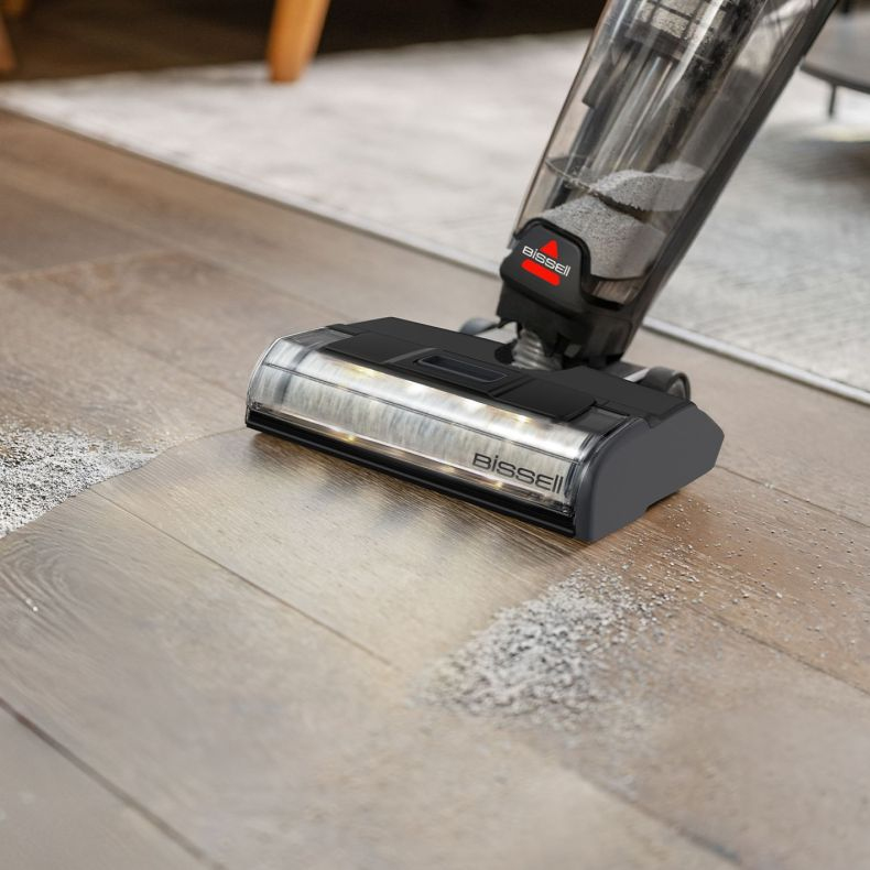 Un aspirapolvere Bissell pulisce i detriti da un pavimento in legno, con spazzola illuminata.