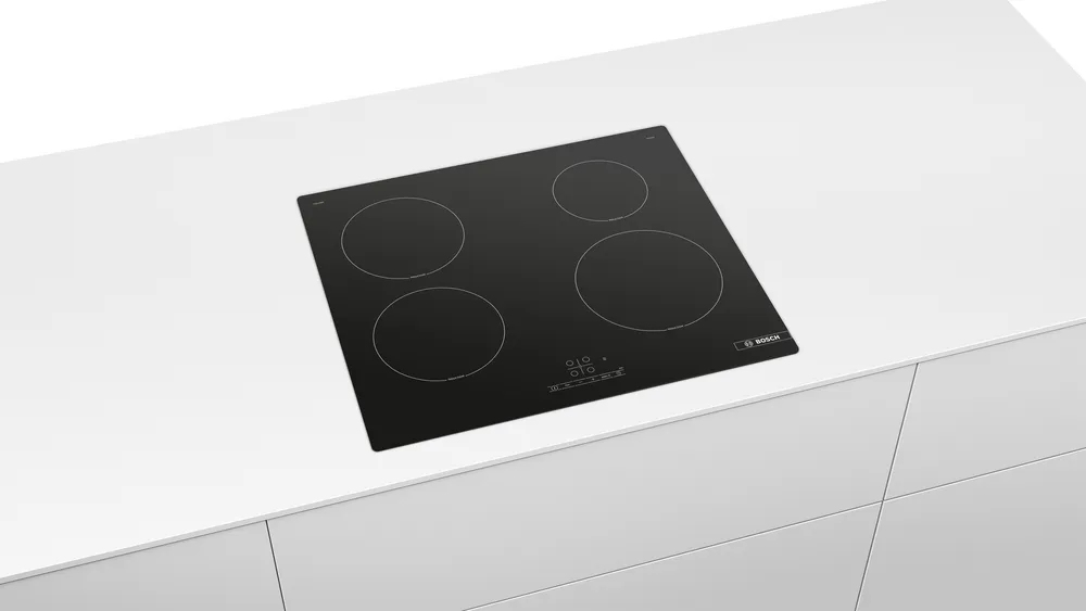 Un piano cottura a induzione nero con quattro zone circolari su un bancone bianco.