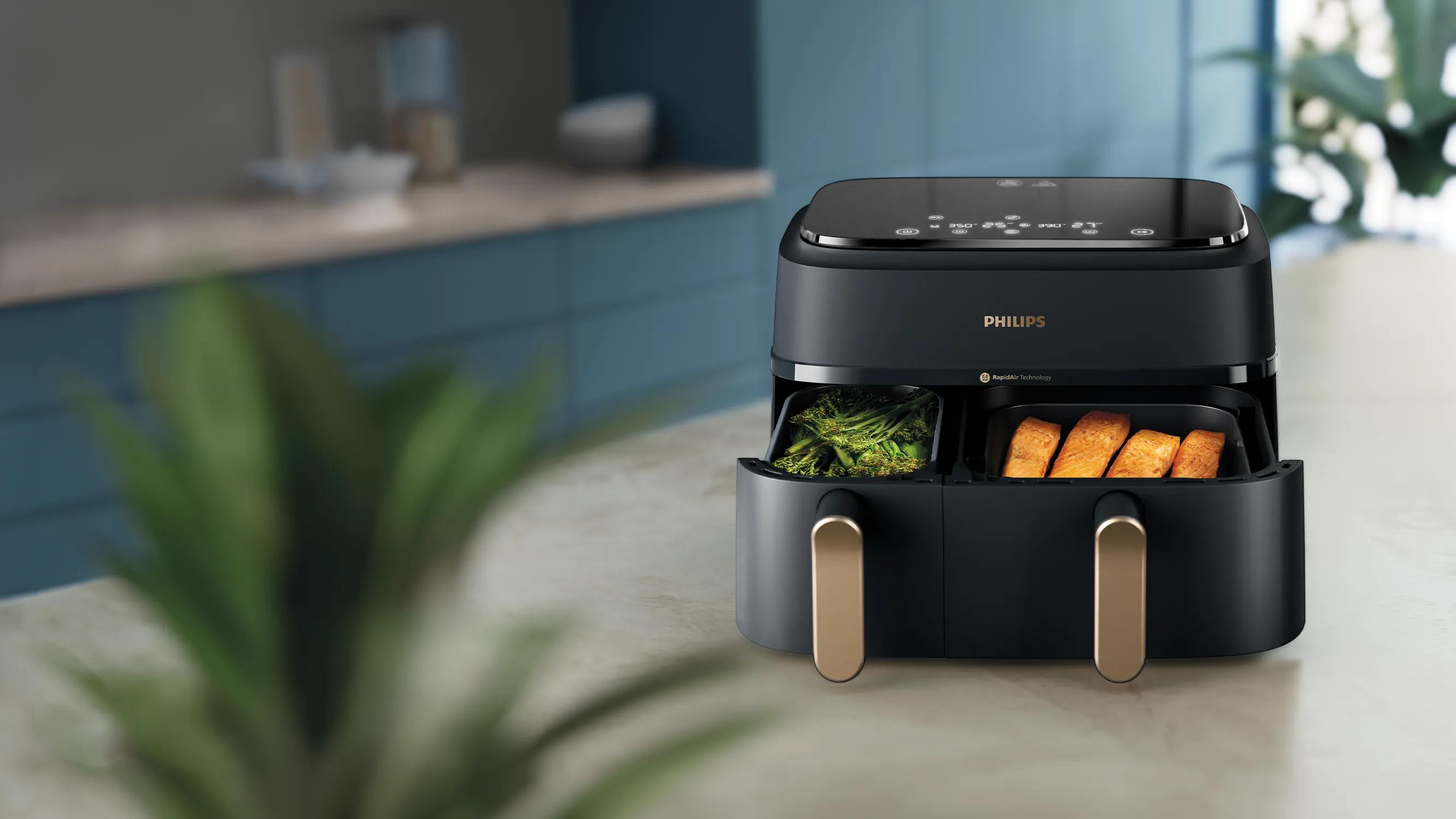 Una friggitrice ad aria nera Philips a doppio cestello sul bancone, con broccoli in un cassetto e salmone nell'altro.