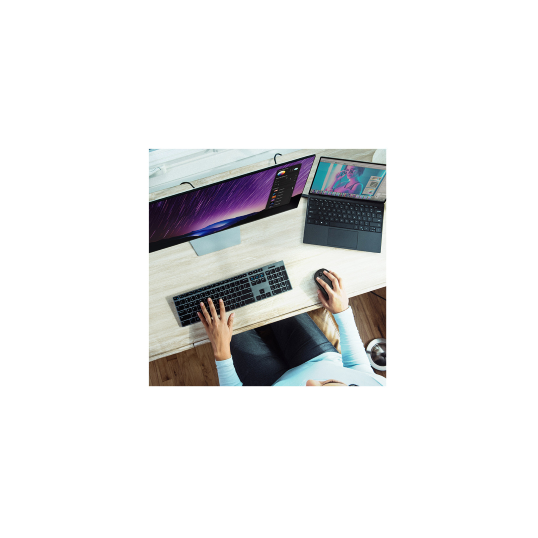 Overhead view of a person typing on a keyboard and using a mouse at a desk with a monitor and laptop.