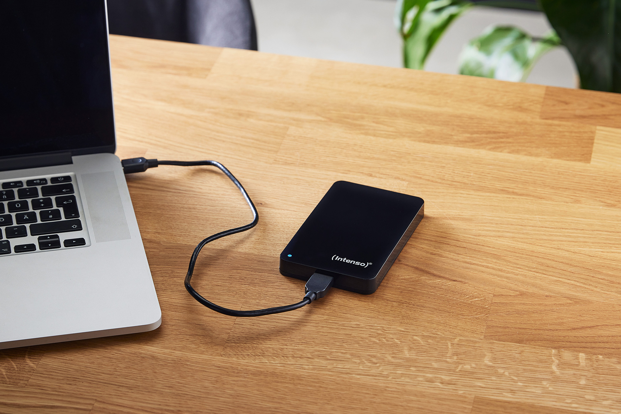 Eine schwarze Intenso-Festplatte ist über ein Kabel mit einem Laptop auf einem Holztisch verbunden.