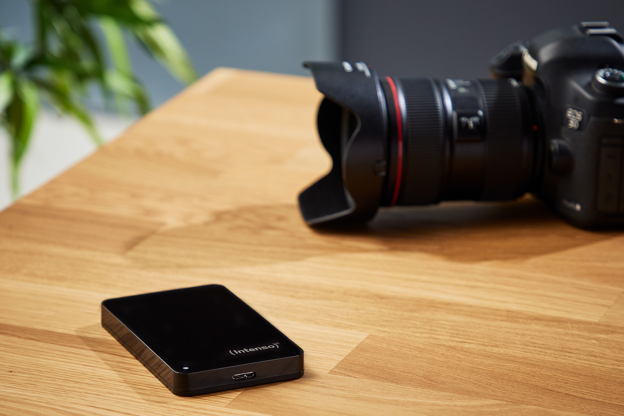 Eine schwarze Intenso-Festplatte und eine DSLR-Kamera liegen auf einem Holztisch.