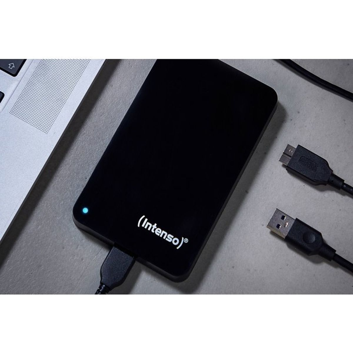 Eine schwarze Intenso externe Festplatte mit USB-Kabel auf einem Schreibtisch neben einem Laptop.