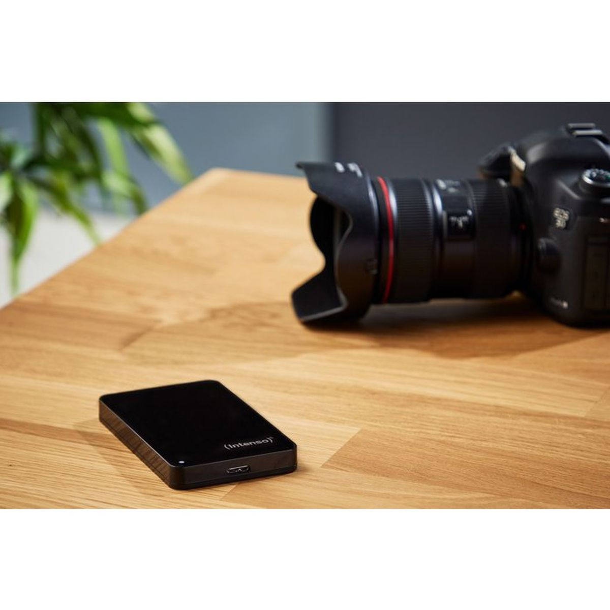 Eine schwarze externe Festplatte von Intenso liegt auf einem Holztisch neben einer DSLR-Kamera.