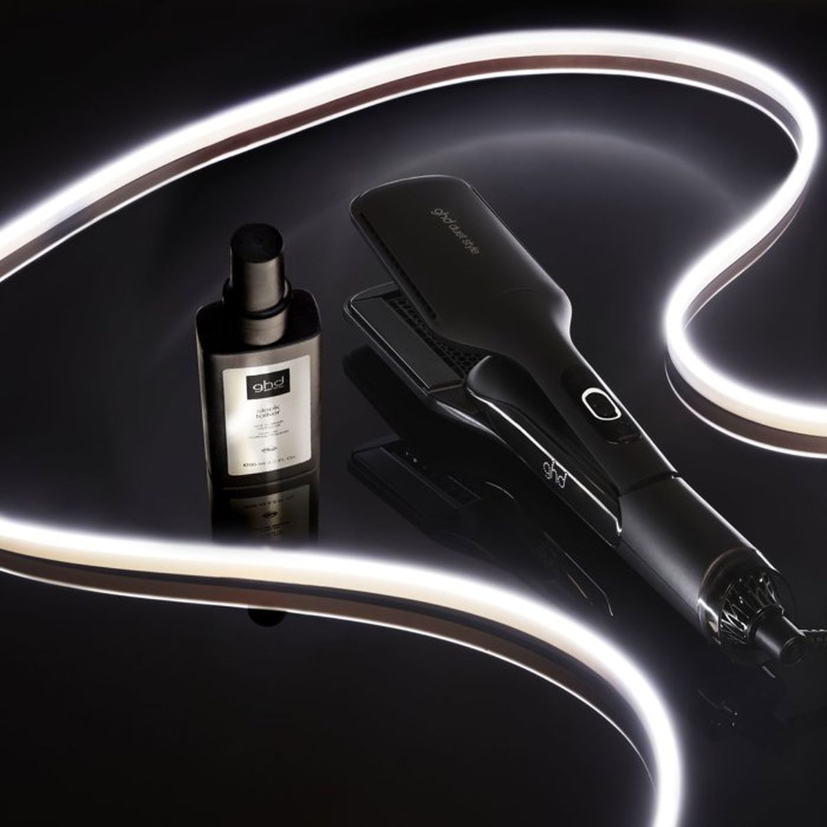 Ein schwarzer ghd Haarstyler und Stylingprodukt auf dunkler, reflektierender Oberfläche, umrahmt von Leuchtstreifen.