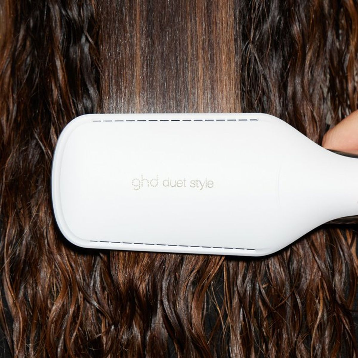 Eine weiße ghd duet style Haarglättungsbürste glättet nasses braunes Haar.