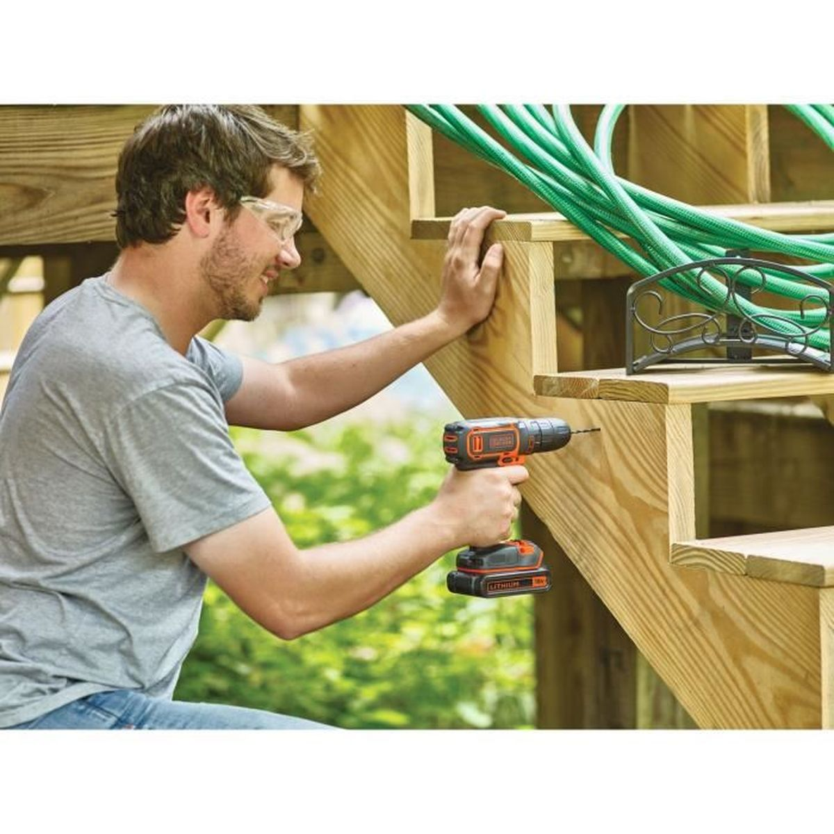 Ein Mann mit Schutzbrille nutzt einen Akkuschrauber, um an einer Holztreppe zu arbeiten.