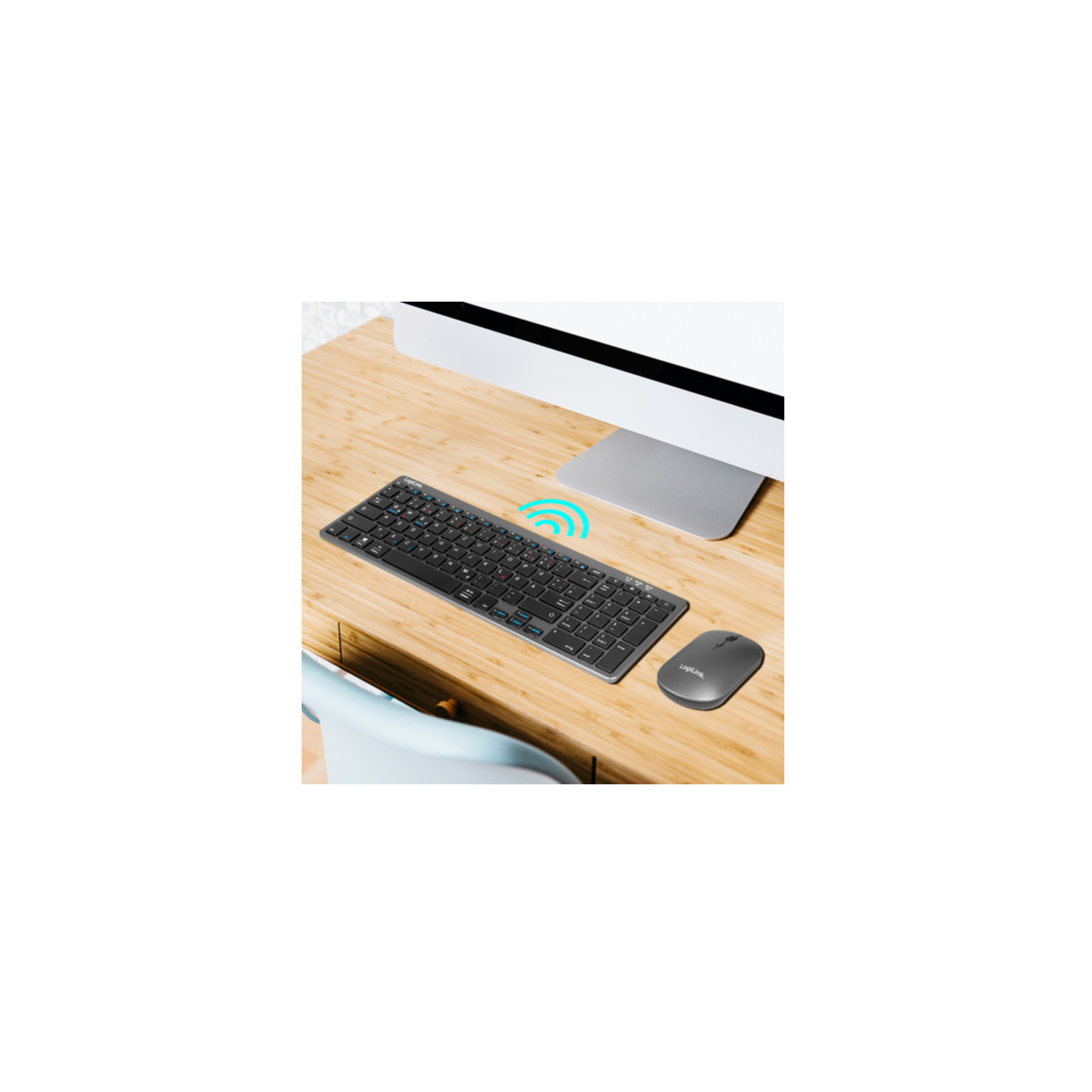Tastiera e mouse wireless su una scrivania in legno chiaro con monitor e sedia blu.