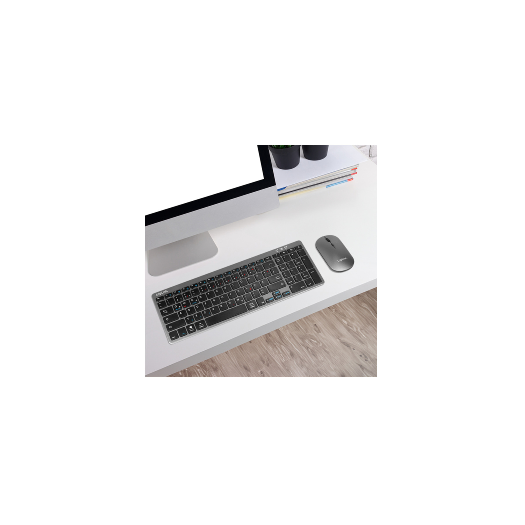 Una scrivania bianca con monitor, tastiera grigia, mouse grigio e riviste.